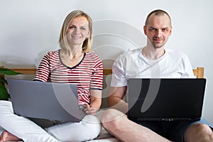 Young family works remotely from home on bed at the computer. Quarantined couple coronavirus. Stay home safe. Distance