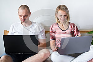 Young family works remotely from home on bed at the computer. Quarantined couple coronavirus. Stay home safe. Distance