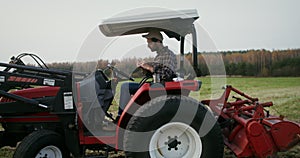 Young farmer eating sandwich sitting in the open cabin of agricultural machine