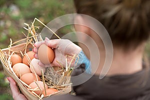 A young farmer female holding a fresh hen egg and other eggs in