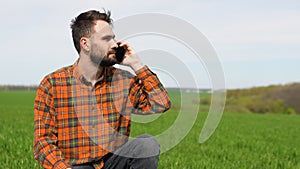 Young farmer in filed examining wheat growing and talking at phone