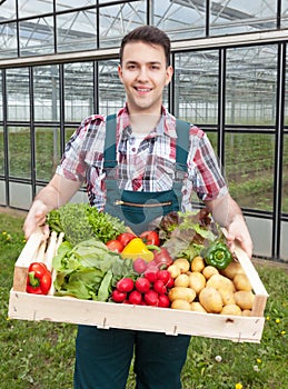 Young farmer in front of a greenhouse with vegetables