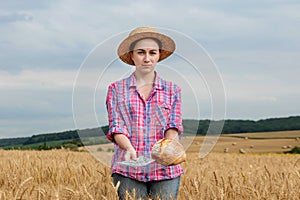 Young farmer holding dollars and bread in golden wheat field. Profit from agriculture during harvesting season in the