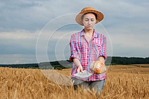 Young farmer holding dollars and bread in golden wheat field. Profit from agriculture during harvesting season in the