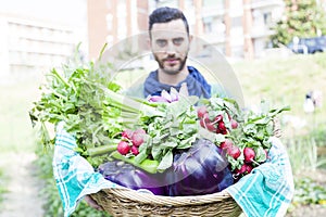 Young farmer showing a basket of vegetables in his garden