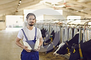 Young farmer standing in feedlot barn holding bottles of natural milk manufactured on his farm