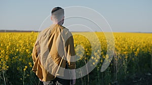 A young farmer walks along a blooming rapeseed field, rear view