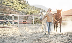 Young farmer woman preparing her horses for training - Cowgirl having fun in ranch farm outdoor - Concept about love between