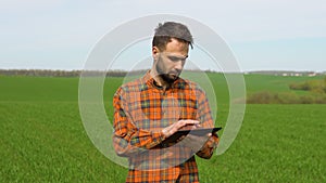 Young farmer working in a wheat field, inspecting and tuning irrigation center pivot sprinkler system on tablet