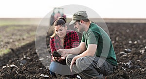 Young farmers exam dirt while tractor is plowing field