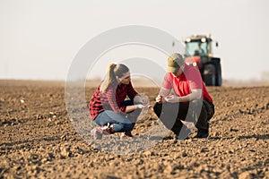 Young farmers examing planted wheat while tractor is plowing fi