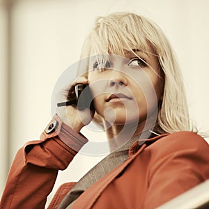 Young fashion blond business woman in red jacket calling on cell phone