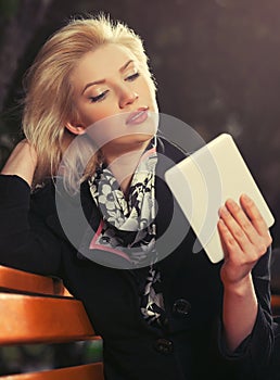 Young fashion blond business woman using digital tablet computer on bench