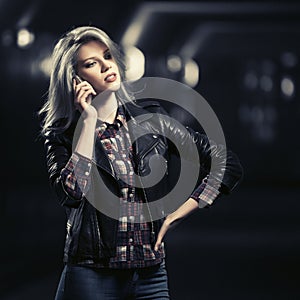 Young fashion blond woman in leather jacket calling on cell phone