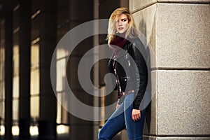 Young fashion blond woman in leather jacket at the wall