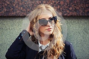 Young fashion blond woman in sunglasses at the wall