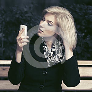 Young fashion blond woman using smart phone in city street