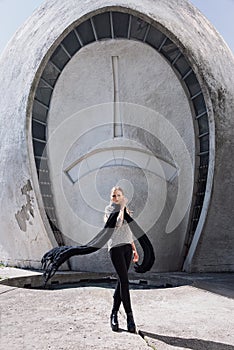 Young fashion blonde girl wearing long black scarf on the background of the futuristic building.