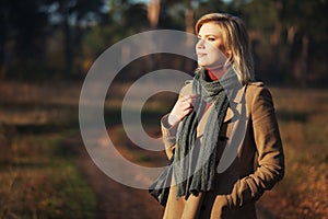 Young fashion blonde woman in beige coat and gray scarf walking outdoor