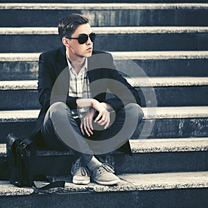 Young fashion business man in sunglasses sitting on the steps