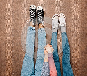 Young fashion couple's legs in jeans and sneakers feet up and holding hands on the wall. Close up. Warm color. Indoor.