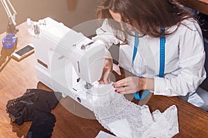 Young fashion designer stitching delicate lace on sewing machine sitting in workshop.