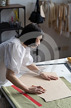 Young fashion designer in studio work on patterns. Girl dressmaker fit drafts and fabric to sketch