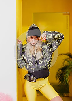 Young fashion girl blogger with black cap on the head dressed in a stylish black and yellow jacket and yellow shorts