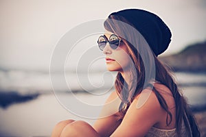 La moda retrato de joven hipster mujer con sombrero y gafas de sol en la playa al atardecer, de estilo retro tonos de color.