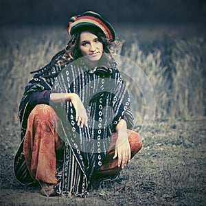 Young fashion hipster woman in rasta poncho sitting on the ground