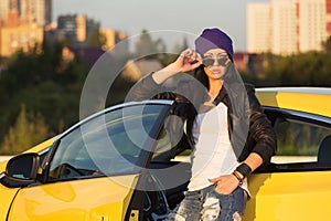 Young fashion hipster woman in ripped jeans leaning on her car