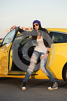 Young fashion hipster woman in ripped jeans leaning on her car
