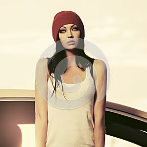 Young fashion hipster woman in white tank top standing beside her car