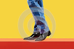 Young fashion man's legs in blue jeans and black boots on red floor