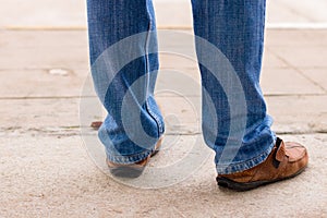 Young fashion man`s legs in blue jeans and brown boots on concre