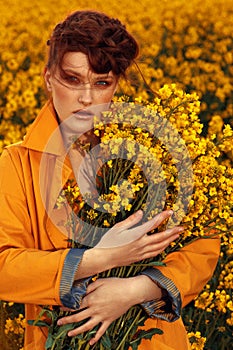 Young fashion model portrait with ginger hair and blue eyes in yellow rapeseed field.