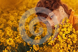 Young fashion model portrait with ginger hair and blue eyes in yellow rapeseed field.