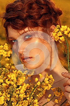 Young fashion model portrait with ginger hair and blue eyes in yellow rapeseed field.