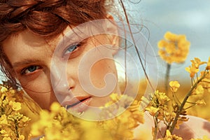 Young fashion model portrait with ginger hair and blue eyes in yellow rapeseed field.