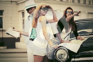 Young fashion people with a road map next to vintage car