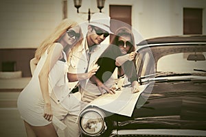 Young fashion people with a road map next to vintage car