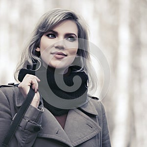 Young fashion woman in beige coat walking in autumn city park