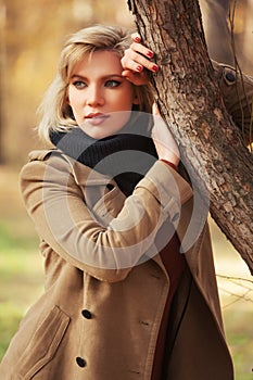Young fashion woman in beige coat walking in autumn park