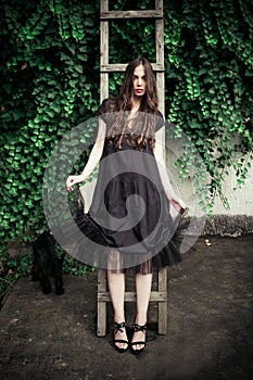 Young fashion woman in black elegant dress lean on wooden ladder