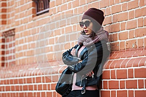 Young fashion woman in black leather jacket leaning on brick wall