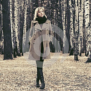 Young fashion woman in classic beige coat walking in autumn forest