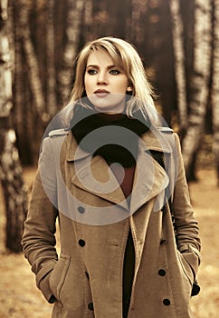 Young fashion woman in classic beige coat walking in autumn park