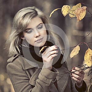 Young fashion woman in classic beige coat walking in autumn park