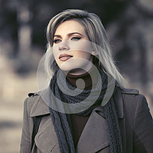 Young fashion woman in classic beige coat walking in autumn park