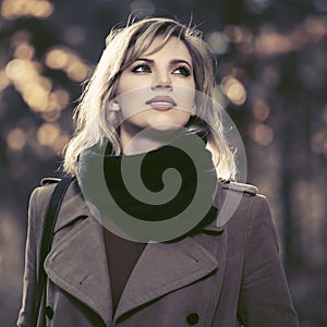 Young fashion woman in classic beige coat walking in autumn park